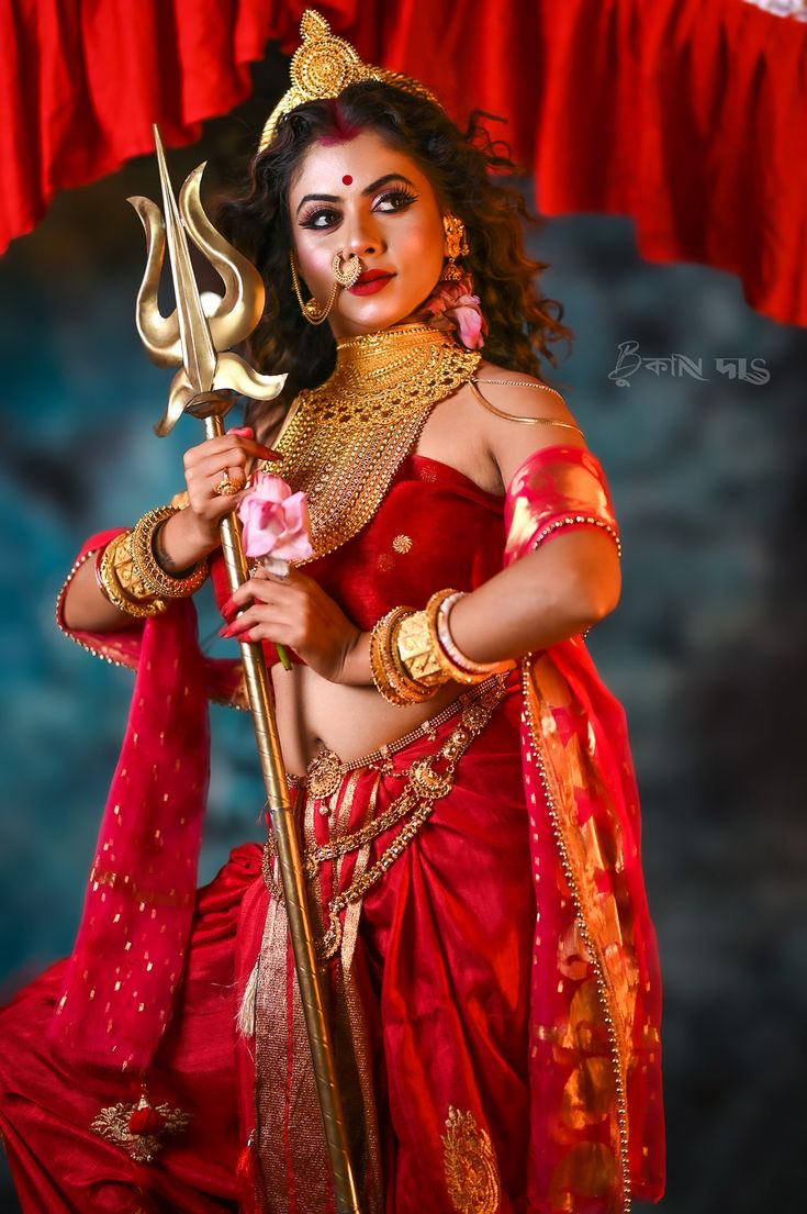 a woman dressed in red and gold holding a spear