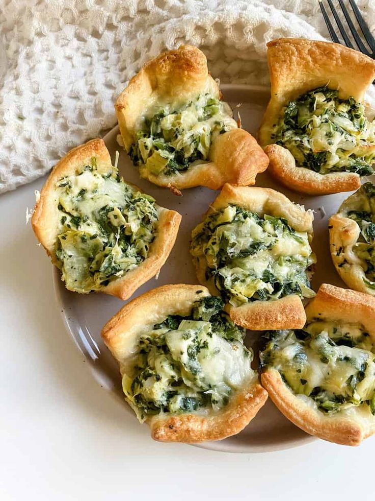 a white plate topped with mini spinach and cheese pies next to a fork