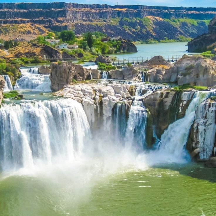 the waterfall is surrounded by large rocks and green water, with a bridge in the background