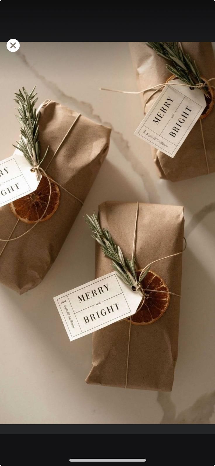 three wrapped gift bags with rosemary tied to them and the words merry bright written on each package