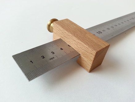 there is a wooden ruler with a metal blade on it's end and a measuring tape in front of it