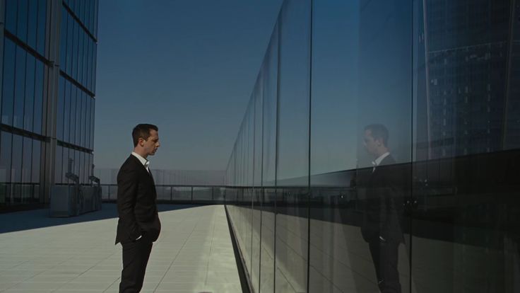 a man in a suit standing next to a glass wall and looking at the camera