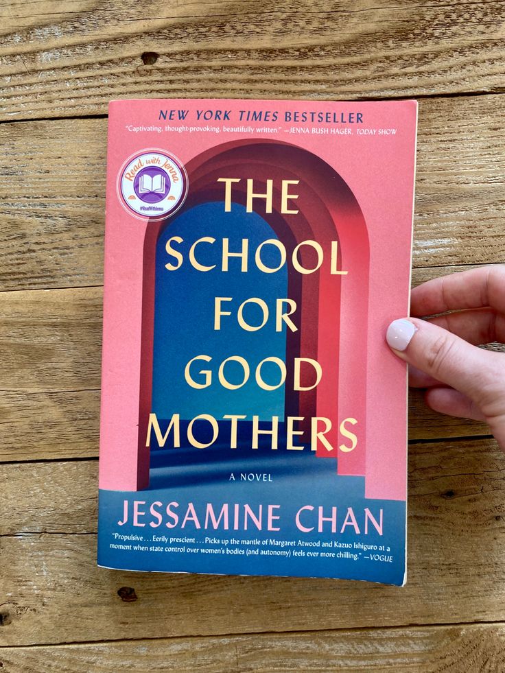 a person holding up a book about the school for good mothers on a wooden table