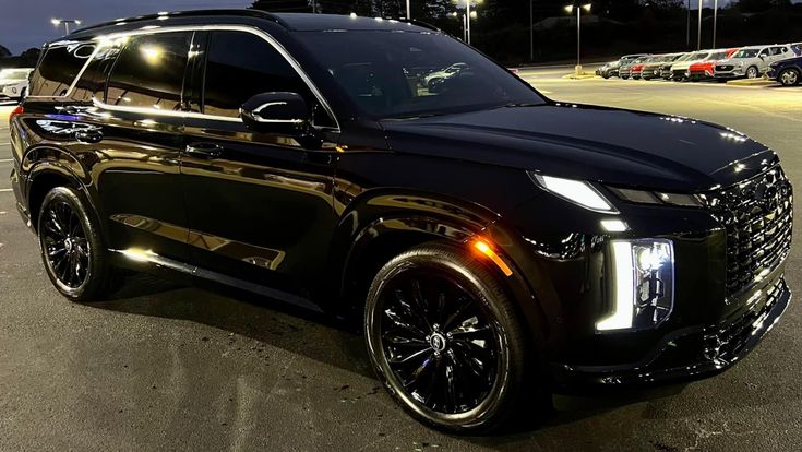 a black suv is parked in a parking lot at night with other cars behind it