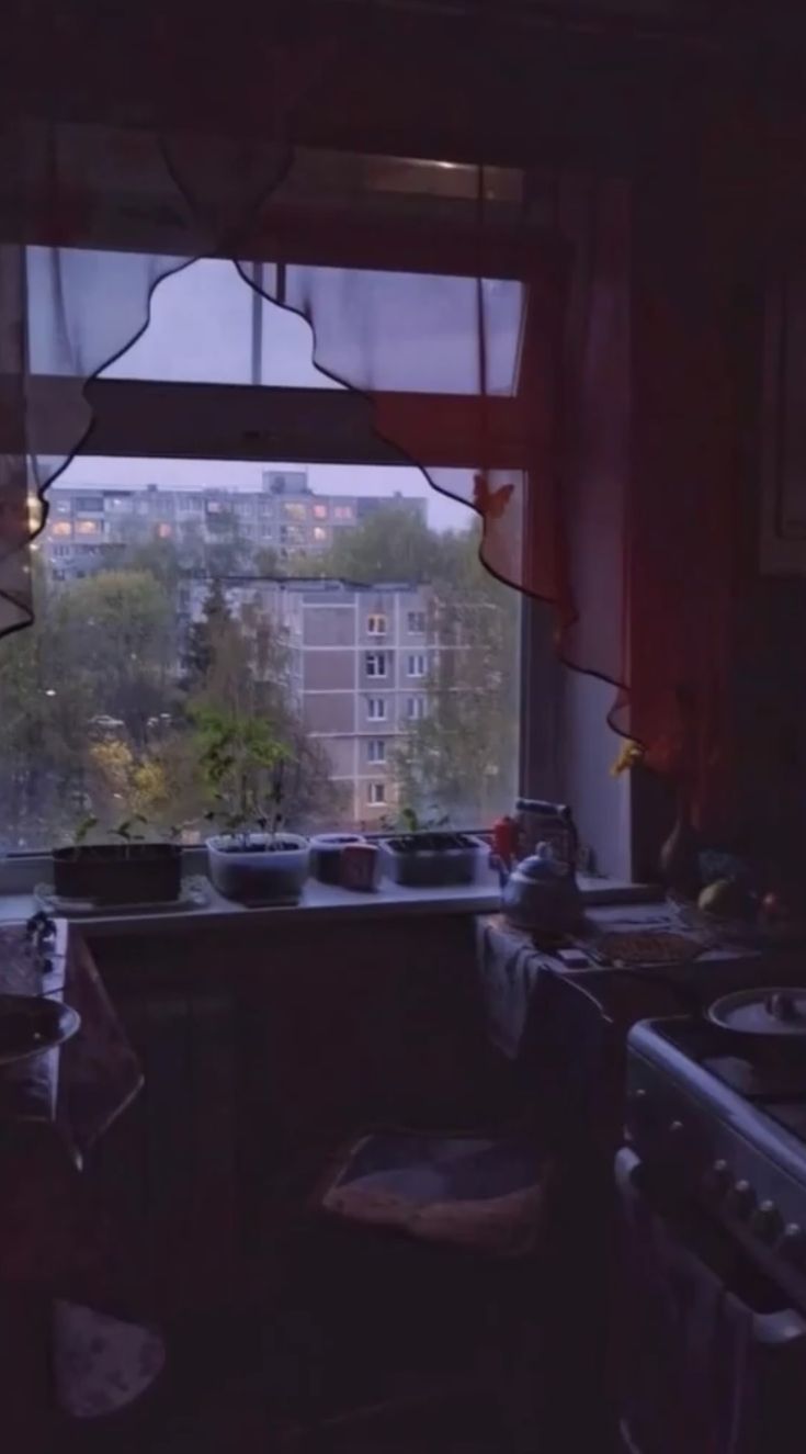 a kitchen with an open window looking out at the city outside in the evening time