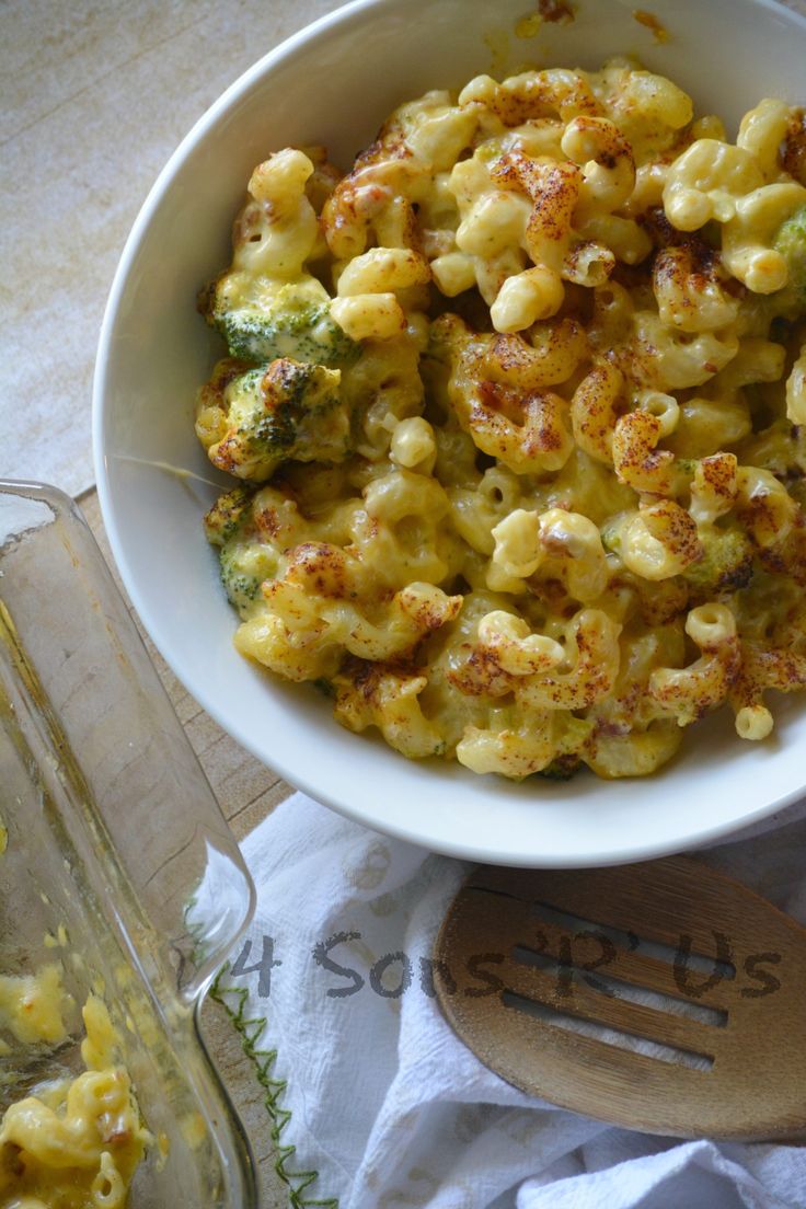 a white bowl filled with macaroni and cheese next to a glass dish full of broccoli