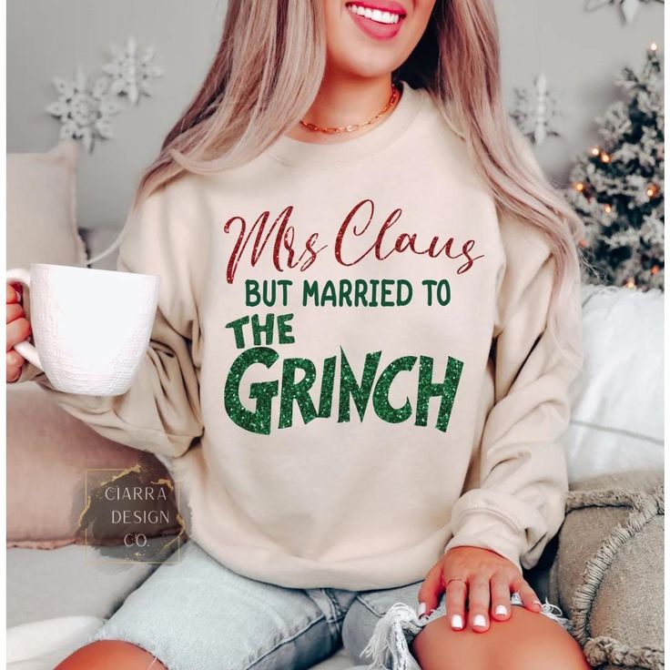 a woman sitting on a couch holding a coffee cup and wearing a sweatshirt that says, mrs claus but married to the grin