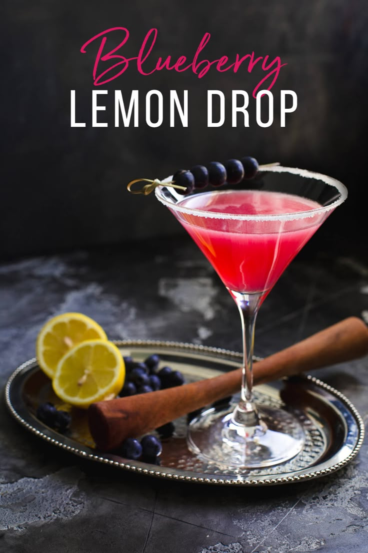 a red drink in a martini glass with blueberries and lemons on the side