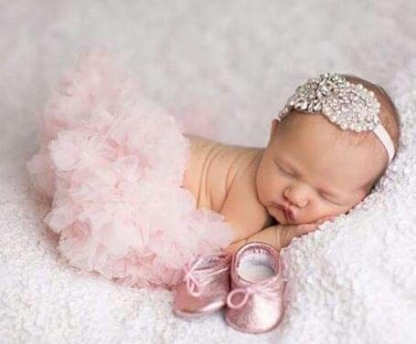 a baby girl wearing a pink tutu and a tiara sleeping on a white blanket