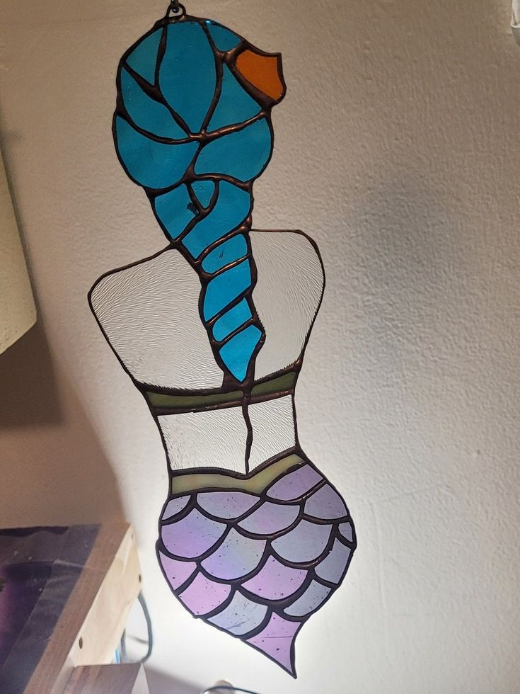 a stained glass mermaid's tail hanging from the ceiling in a room with white walls