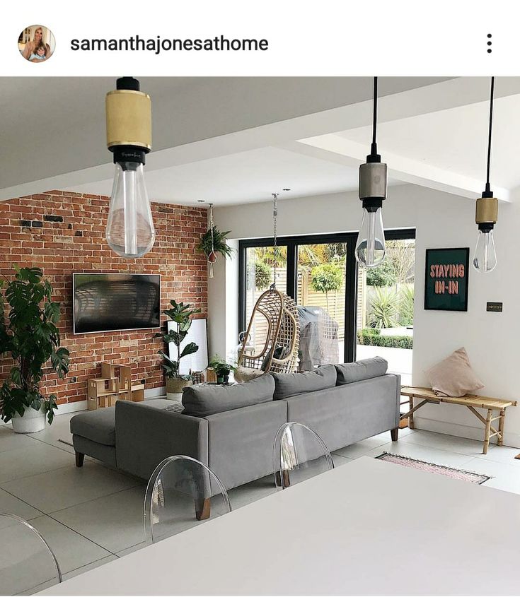 a living room filled with furniture next to a brick wall covered in plants and hanging lights