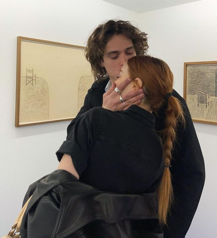 a woman with red hair is hugging another woman's face in an art gallery