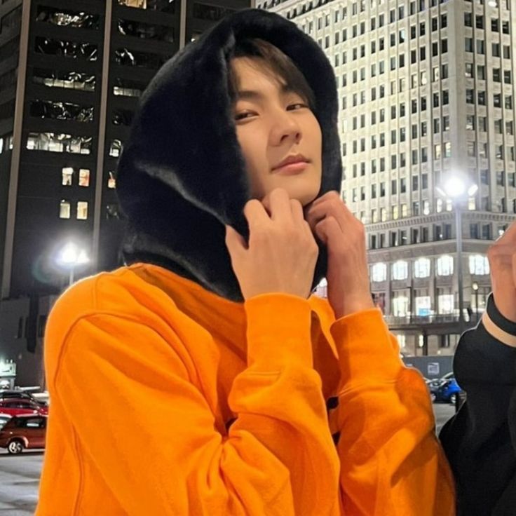 a young man in an orange hoodie is standing on the street with his hands to his face