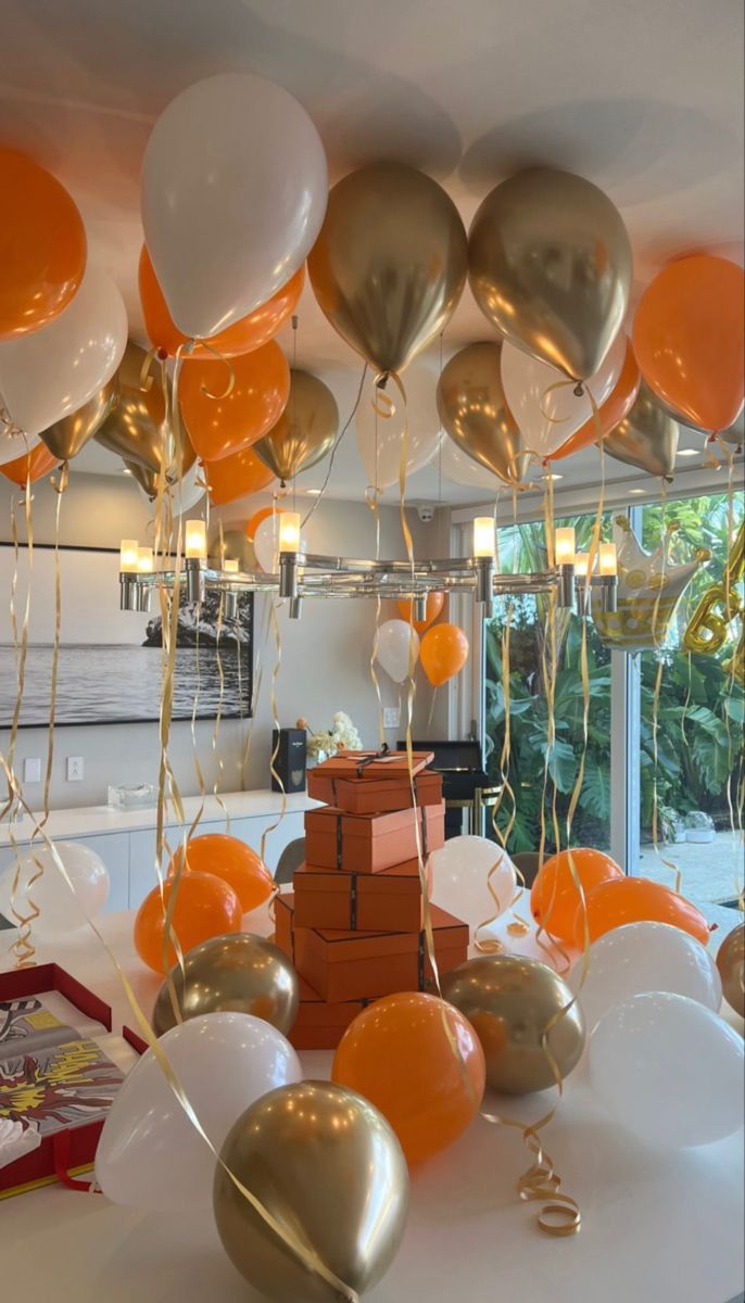 balloons and streamers are hanging from the ceiling above a table with boxes on it