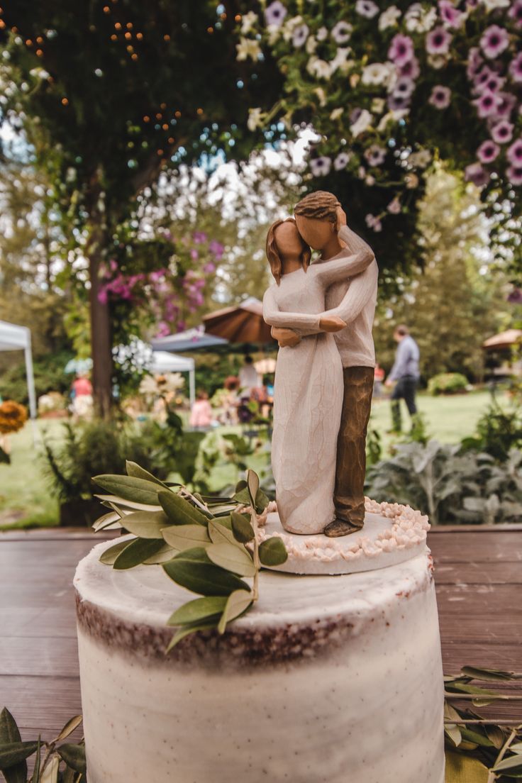 a wedding cake with a figurine of a couple kissing on top and flowers in the background