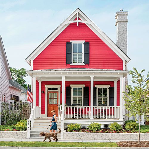 a woman walking her dog down the street in front of a red house with white trim