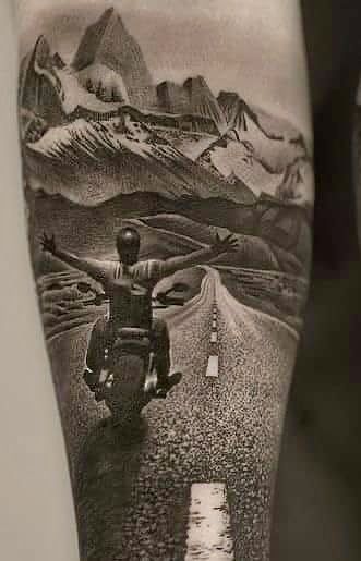 a black and white photo of a person riding a motorcycle on a road with mountains in the background