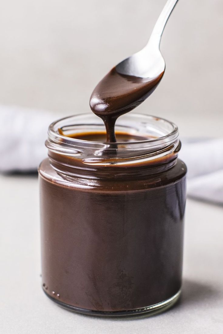 a spoon full of chocolate spread on top of a jar filled with melted chocolate sauce