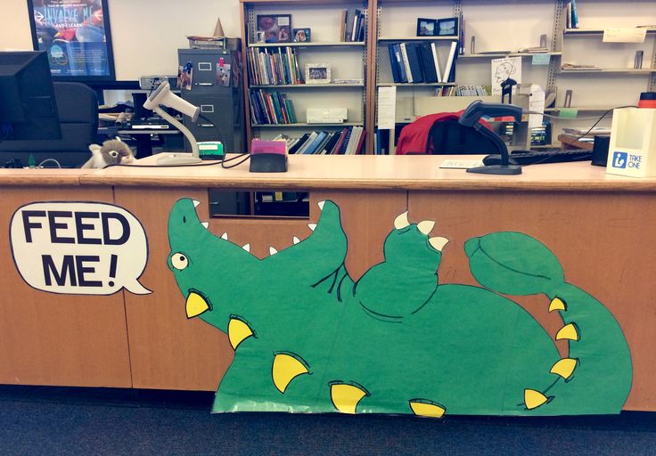 an office cubicle decorated with a green dinosaur and feed me sign on the front