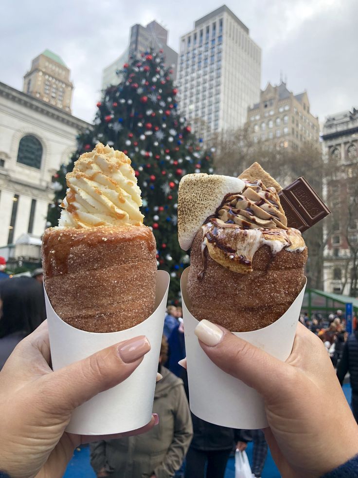 two people holding up ice cream cones in front of a christmas tree at rockefeller square