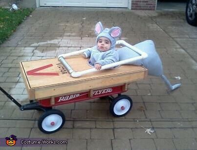 a baby in a mouse costume riding on top of a wagon with wheels and ears