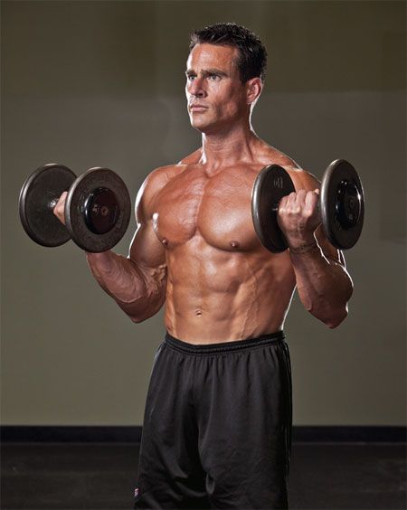 a shirtless man holding two dumbbells in his hands