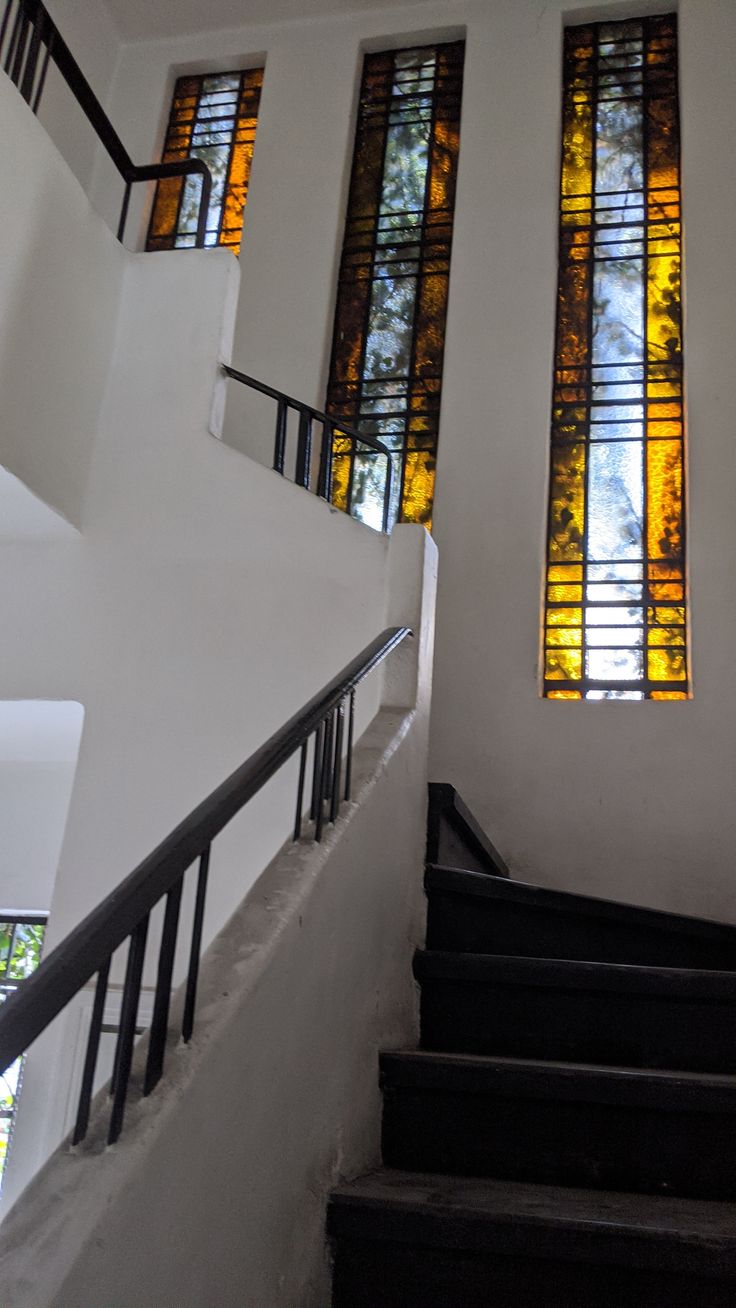 stairs leading up to three stained glass windows in a building with white walls and black handrails