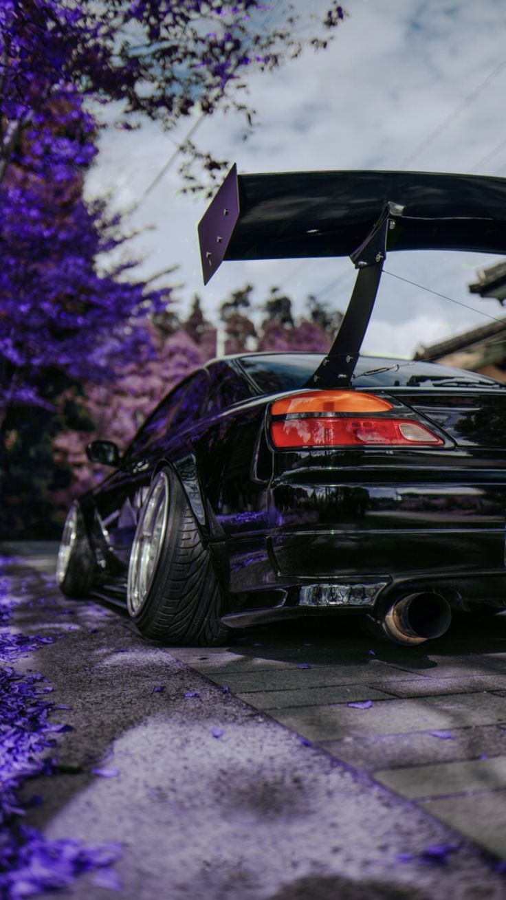 the back end of a black car parked in front of purple trees