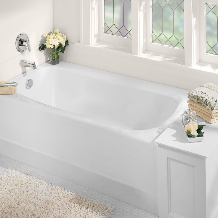 a white bath tub sitting on top of a rug next to a sink and window