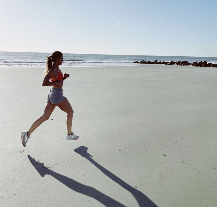 a woman is running on the beach with her shadow in the sand and water behind her