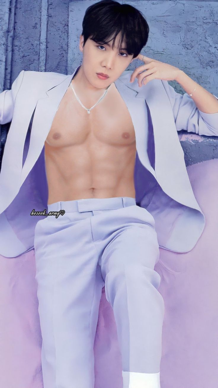 a shirtless man sitting on top of a bed wearing blue pants and white shoes