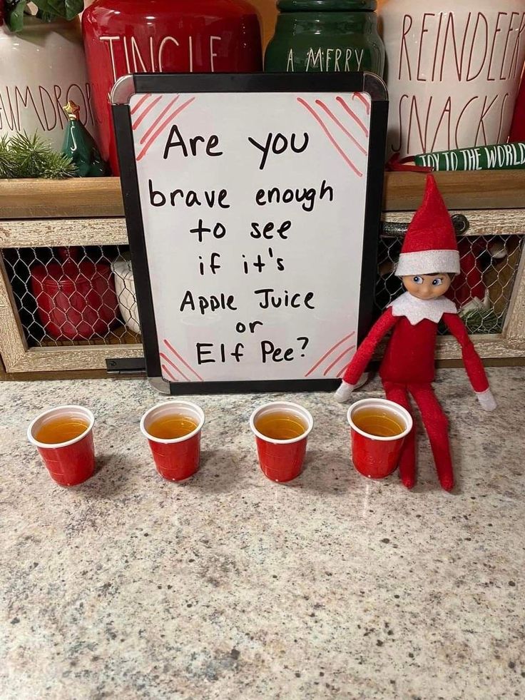 an elf with four cups of tea next to a sign that says are you brave enough to see if apple juice or elf pez?