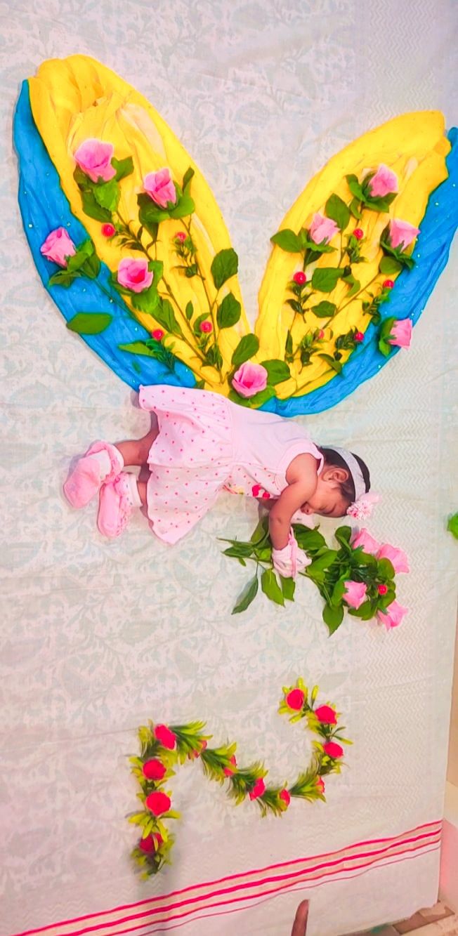 a baby laying on top of a bed next to pink roses and green leaves in the air