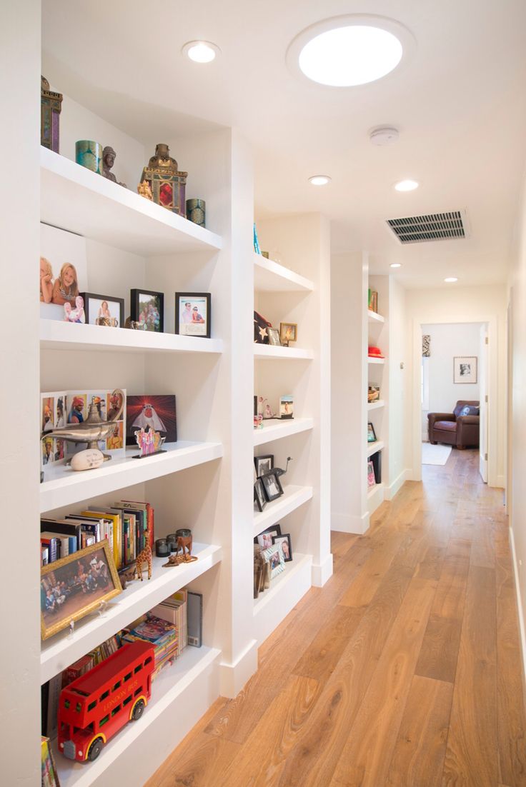 an empty room with white shelving and wooden floors in the center is filled with toys