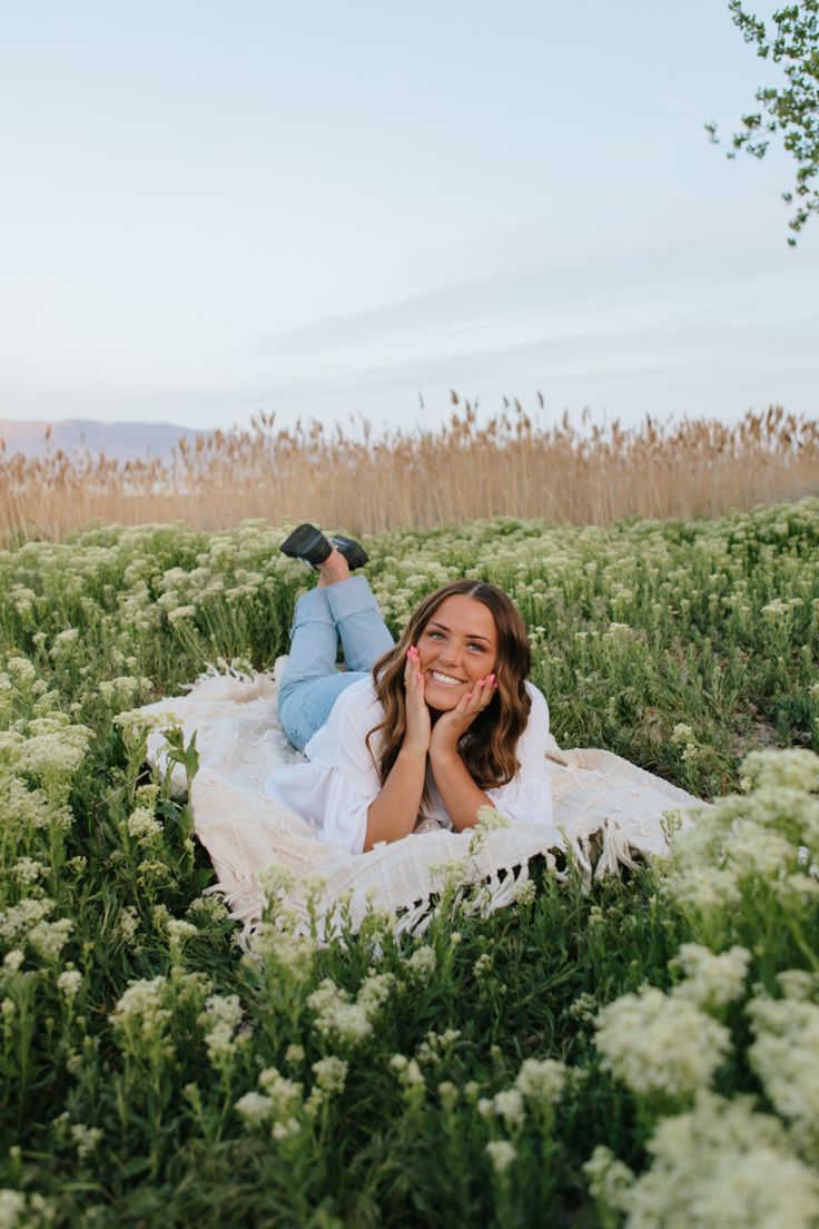 a woman laying on top of a blanket in a field with tall grass and flowers