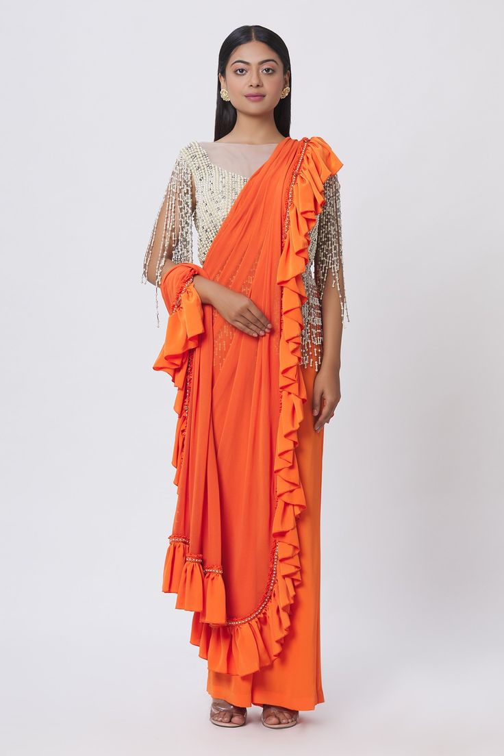 Orange pre-draped saree with ruffle detail and pearl embellishment on the border. Comes with pearl embellished blouse.
Components:2
Pattern:Embellishment
Type of Work:Pearl and Stone
Neckline:Boat
Sleeve Length:Sleeveless
Fabric:Lycra
Color:Orange
Other Details:
Mesh detail on the neckline
Tassel fringe detail
Closure: Blouse: Back zip; Saree: Side zip
Occasion:Party - Aza Fashions Silk Saree With Ruffles For Evening, Evening Blouse Piece With Ruffles For Diwali, Diwali Evening Blouse Piece With Ruffles, Evening Diwali Blouse Piece With Ruffles, Diwali Evening Ruffled Blouse Piece, Evening Ruffled Blouse Piece For Diwali, Designer Georgette Pre-draped Saree With Ruffles, Ruffled Georgette Saree In Traditional Drape, Ruffled Georgette Saree With Traditional Drape