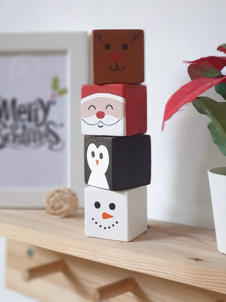 three wooden blocks with faces on them sitting on a shelf next to a potted plant