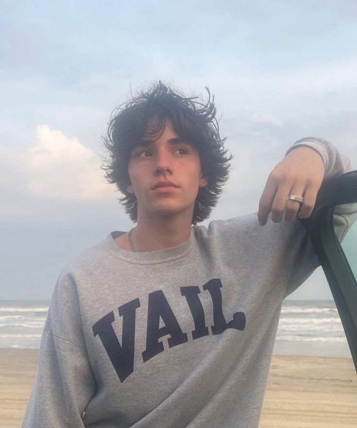 a young man standing next to a car on the beach with his hand on the window