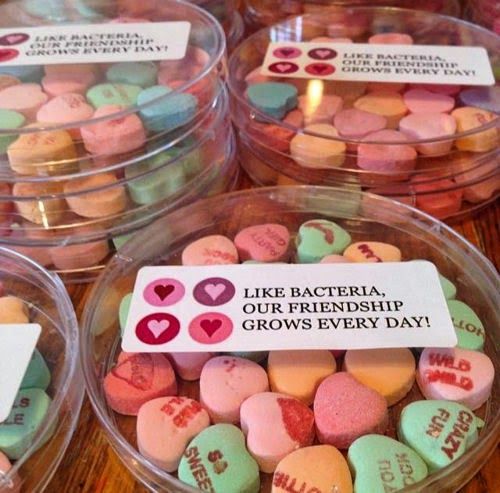 three plastic containers filled with conversation hearts on top of a wooden table next to each other