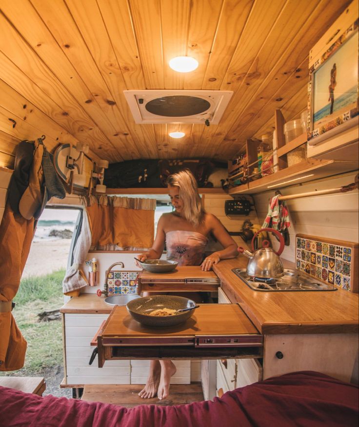 a woman standing in the kitchen of a small camper with her feet on the counter