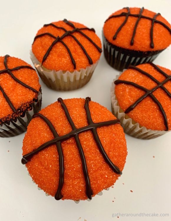 four cupcakes with chocolate drizzled on top and basketball design in the middle