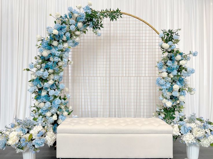 a white and blue wedding arch with flowers on the front, along with a bench for seating