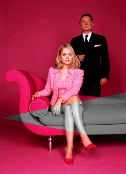 a woman sitting on top of a pink couch next to a man in a suit