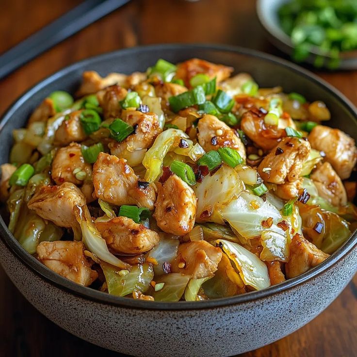 a bowl filled with chicken and vegetables on top of a wooden table