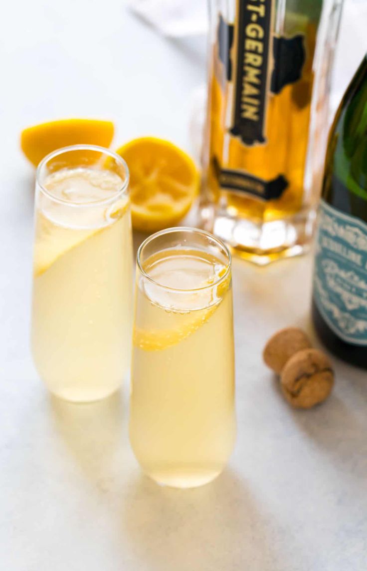 two glasses filled with lemonade next to a bottle of champagne and almonds on a table