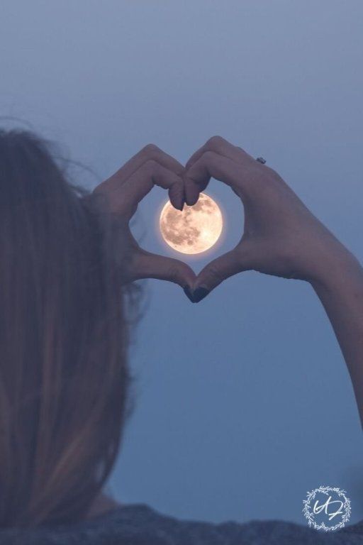 a woman making a heart shape with her hands and the moon in the sky behind her