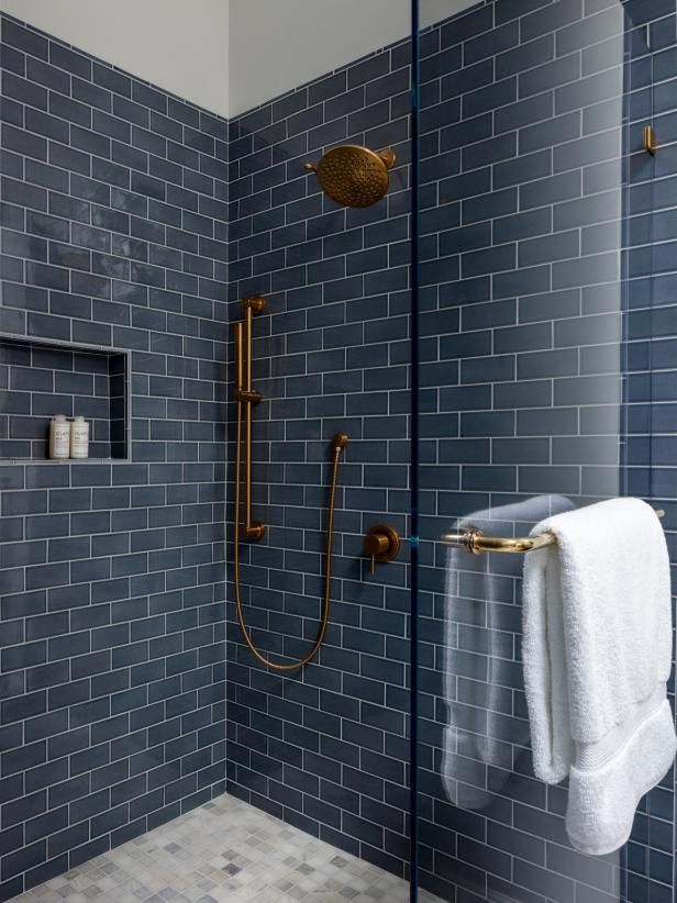 a blue tiled bathroom with gold fixtures and white towels on the shower head, in front of a glass door