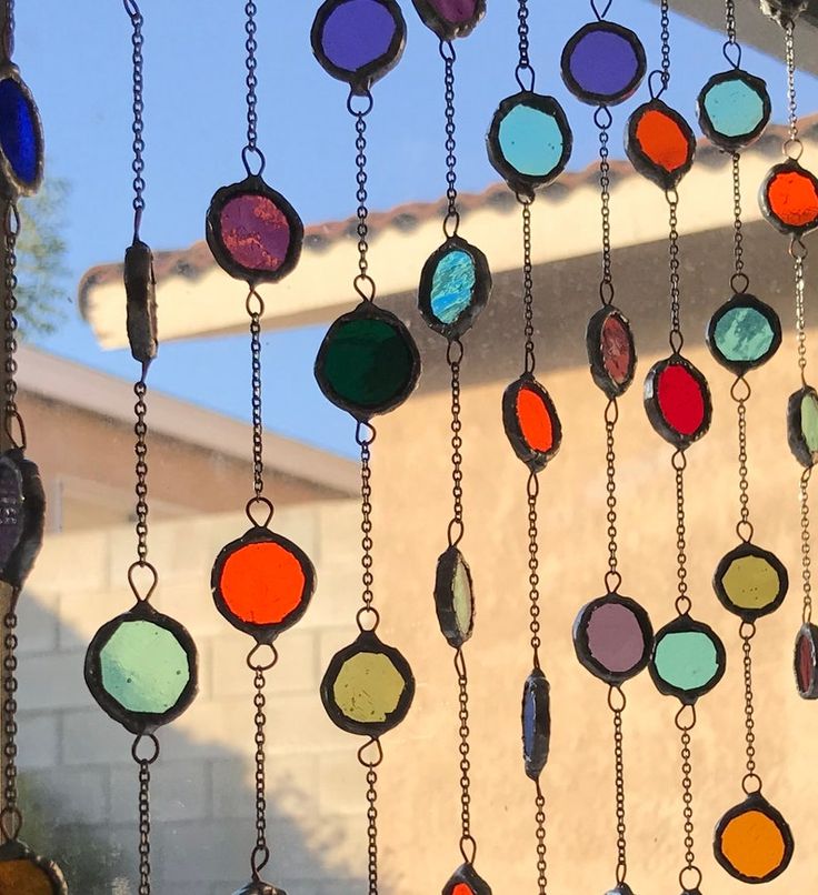 many different colored glass beads hanging from chains on the side of a building with a blue sky in the background