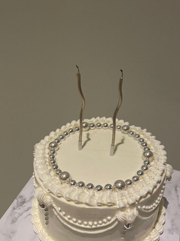 there is a white cake with pearls and two candles on the top, sitting on a marble table