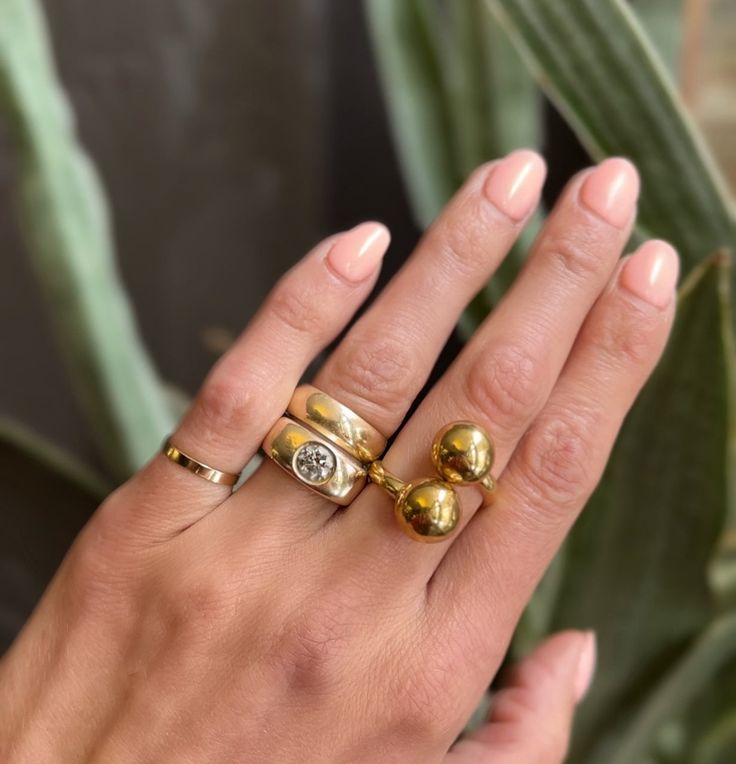 a woman's hand with two gold rings on it and a green plant in the background